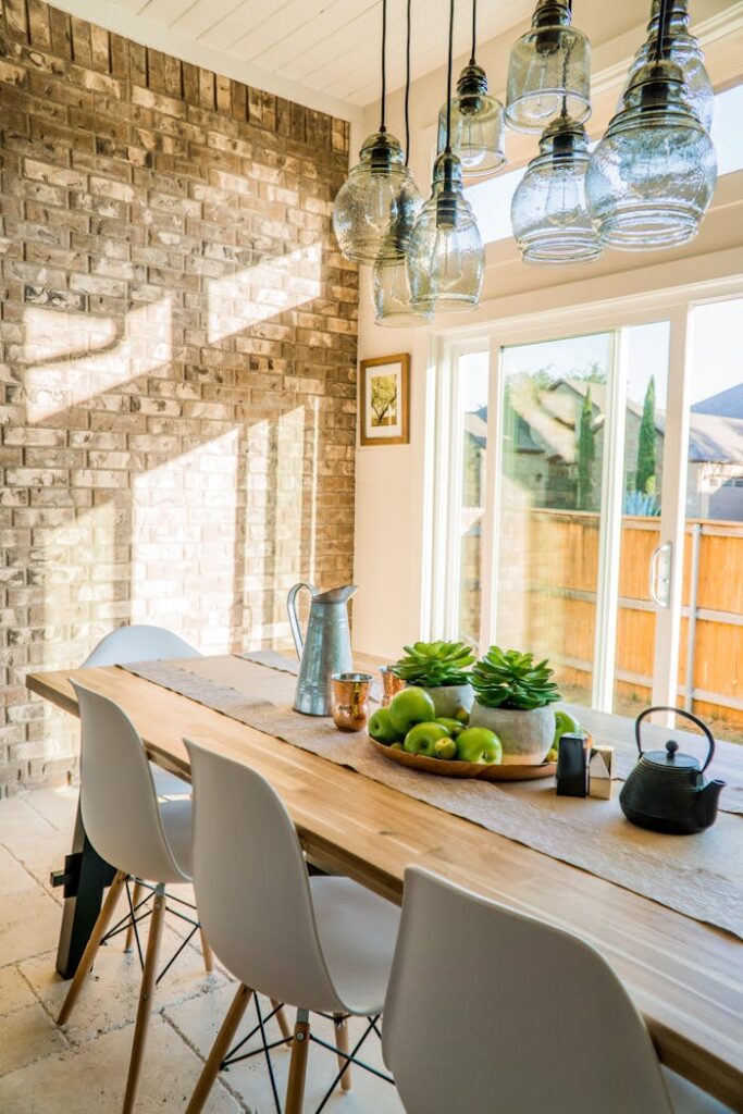 Dlaczego „ciepły” dom może sprzyjać pleśni? Sunlit dining room with contemporary decor and a rustic brick wall, featuring stylish lighting and a wooden table.