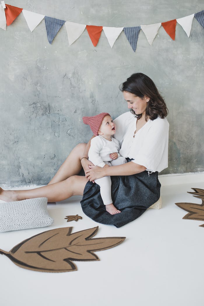 A mother lovingly holds her baby in a cozy room with cardboard leaf decor and hanging flags.